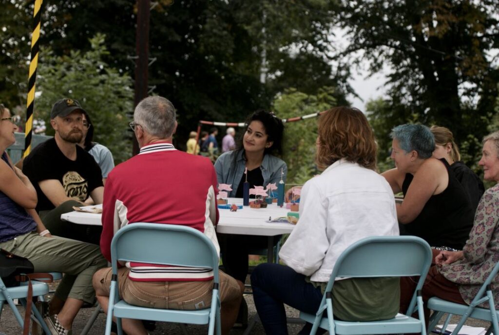 8 people sit around a table outside, in discussion