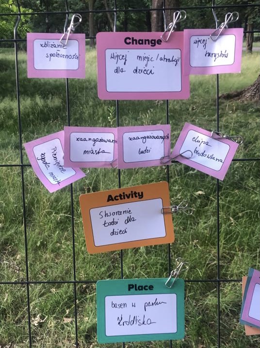Pink, orange and green cards with writing in polish on them, clipped to a metal trellis